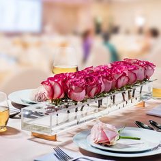 pink roses are placed in a clear vase on a table with plates and silverware