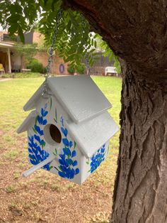 a birdhouse hanging from a tree in the yard with blue flowers painted on it