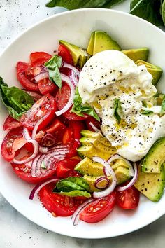 a white bowl filled with salad and dressing on top of a marble table next to sliced avocado