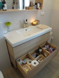 a bathroom with a sink, mirror and toiletries in the cabinet drawer area next to it