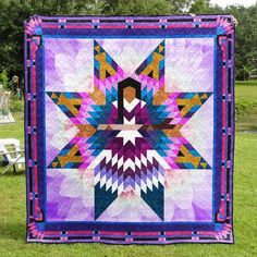 a purple and blue quilt with an abstract star design on the front, sitting in grass