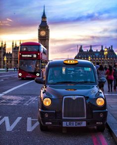 a black taxi cab driving down a street next to a tall clock tower