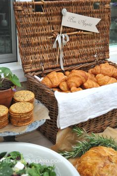 a wicker basket filled with croissants next to potted plants