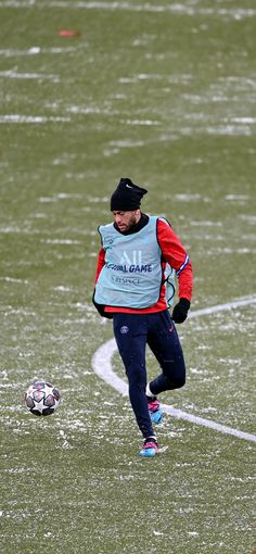 a man kicking a soccer ball on top of a snow covered field in the middle of winter