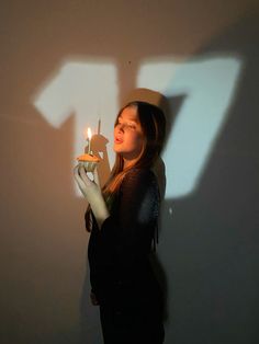 a woman holding a lit candle in front of a wall with the shadow of an arrow on it