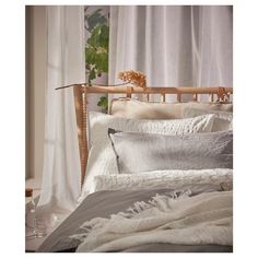 a bed with white linens and pillows in front of a curtained window, next to a wooden headboard