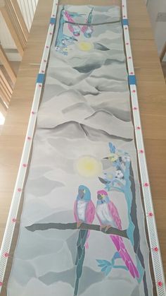 a large painting on the ground with two birds sitting on it's sides and one bird standing on top of another