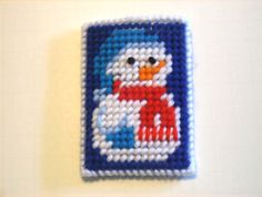 a small square beaded with a penguin on it's face and the words snowman written in red, white, and blue