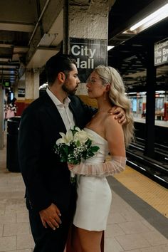 a man and woman standing next to each other in front of a train station platform