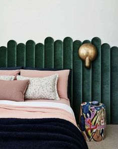 a bedroom with green velvet headboard and pink bedding, gold lamp on the wall