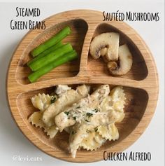 a wooden plate topped with pasta and mushrooms on top of a white table next to green beans