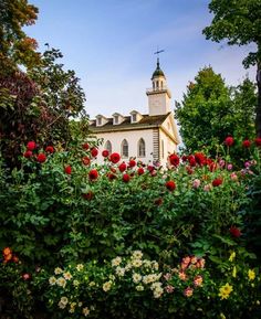 an old church surrounded by beautiful flowers and greenery in the foreground, on a sunny day