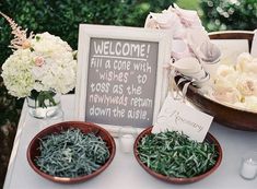 a table topped with two bowls filled with flowers and greenery next to a welcome sign