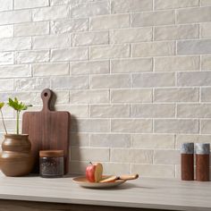 a wooden cutting board sitting on top of a counter next to two vases and an apple