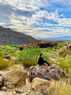 a woman sitting on top of a large rock in the middle of a desert area