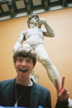 a man standing in front of a statue with his hand up to the camera and making a peace sign