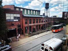 an orange and white bus parked in front of a brick building with people walking on the sidewalk