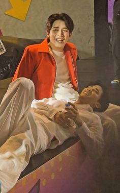 a painting of a man laying on the ground next to another man who is holding a cell phone