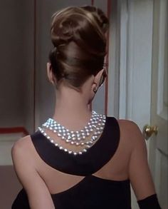 a woman in a black dress with pearls on her neck