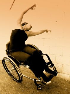 a woman in a wheel chair reaching up into the air with her arms stretched out