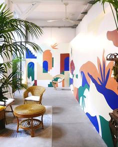 a room filled with lots of plants next to a wall covered in colorful art pieces