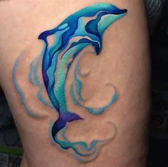 a woman's thigh with a blue dolphin tattoo on her leg and an ocean wave coming out of it