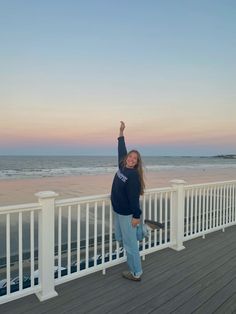 a woman standing on top of a wooden deck next to the ocean with her arms in the air