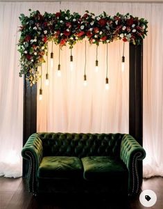 a green couch sitting in front of a wall with flowers and greenery on it