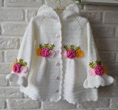 a crocheted sweater with flowers on it hanging from a hook in front of a brick wall