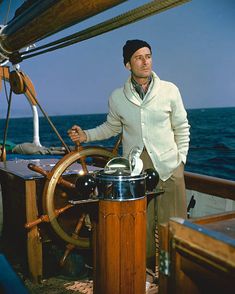 a man standing on the deck of a boat with a steering wheel in front of him