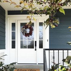 a white door with a wreath on it and some plants in the foreground outside