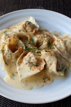 a white plate topped with dumplings covered in sauce and garnished with herbs