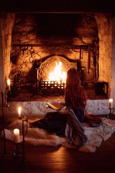 a woman sitting on the floor in front of a fire place with candles around her