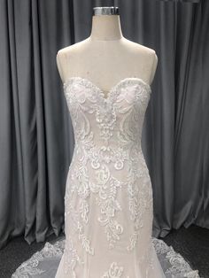 a white wedding dress on display in front of a gray curtained backdrop with sheer lace