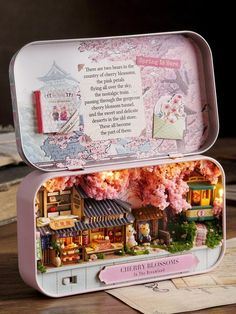 an open tin box with a doll house in it on a table next to books