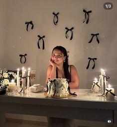 a woman sitting at a table with a cake in front of her and candles on the wall behind her