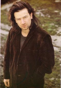 a man with long hair and piercings standing in front of some rocks, looking at the camera