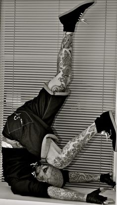 a man with tattoos on his arms and legs doing a handstand in front of a window