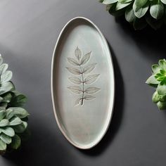 a plate with a leaf design on it next to some plants