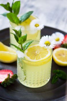 two glasses filled with lemonade and strawberries on a black plate next to flowers