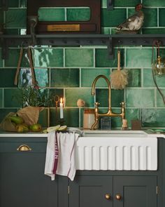 a kitchen with green tiles and gold faucets on the counter top, including a sink