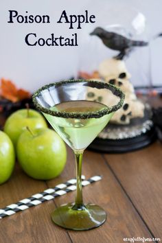 a green drink in a martini glass sitting on top of a table next to apples