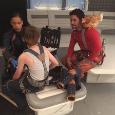 three people sitting on top of a white toilet in front of a window with an orange chicken on his head