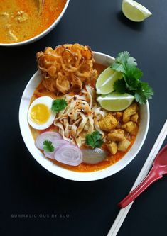 a bowl filled with noodles, meat and vegetables next to a spoon on a table