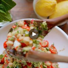 a person is cutting into a salad on a white plate with lemons in the background