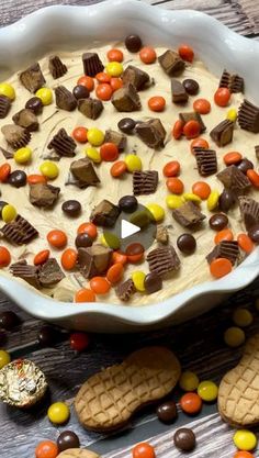 a bowl filled with candy and cookies on top of a wooden table next to crackers