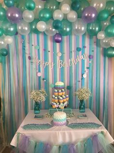 a birthday party with balloons, cake and cupcakes on a table in front of a striped wall