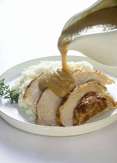 someone pouring sauce on top of some meat and mashed potatoes in a white bowl