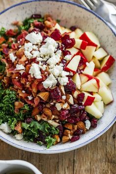 a bowl filled with apples, cranberries, nuts and feta cheese on top of a wooden table