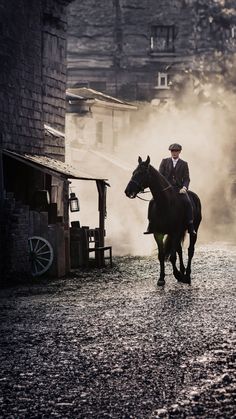 a man riding on the back of a black horse down a street next to a building